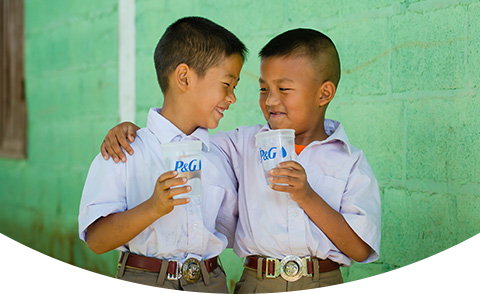 Two smiling schoolboys in uniforms holding clear cups of water with a P&G logo